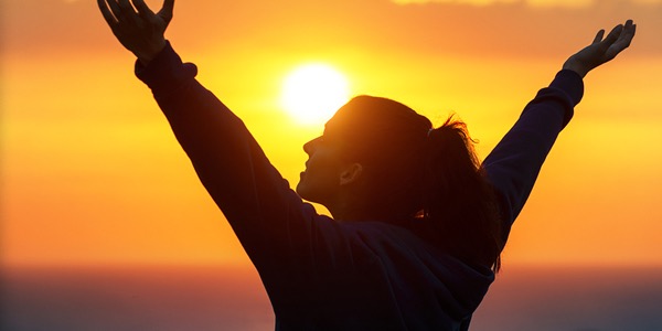 Silhouette of a person raising their arms toward a setting sun